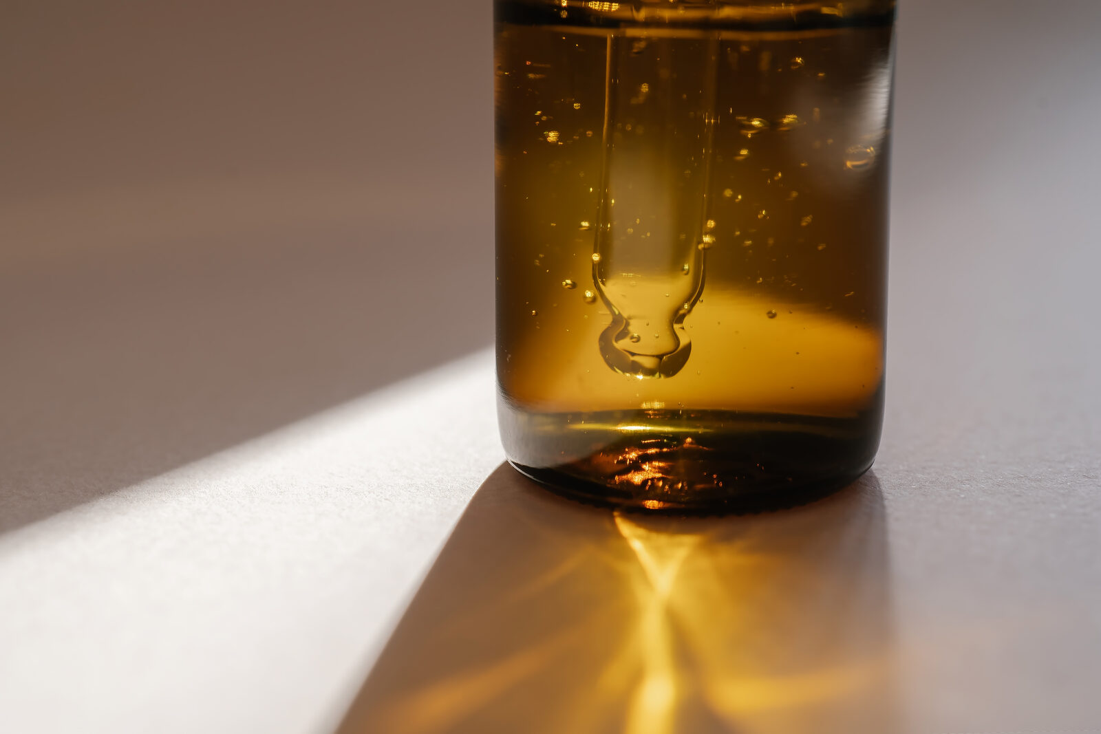 Amberkleurige fles massageolie op een neutrale ondergrond