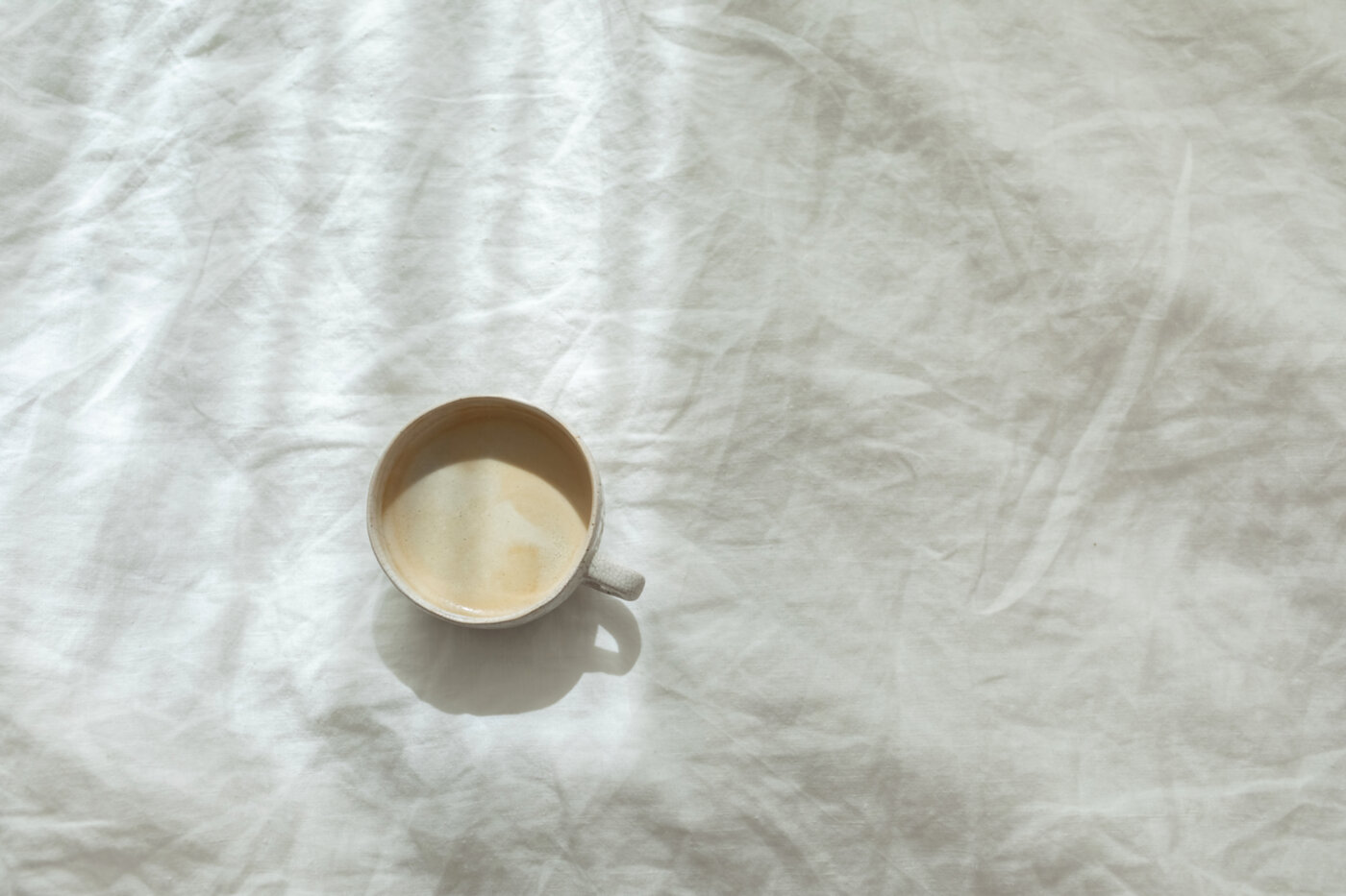 Een koffiekop op zacht wit beddengoed in middaglicht — even langer blijven liggen.